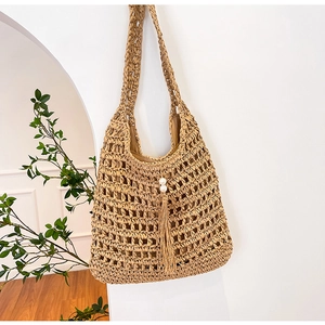 Detail of straw tote bag showing hollow weave texture, pearl charm, and long tassel decoration
