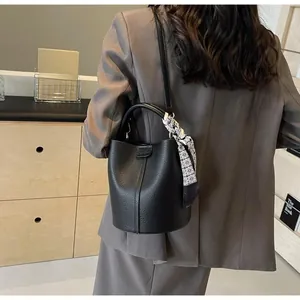 Détail du sac seau en cuir grainé noir avec poignée ornée d'un foulard en soie