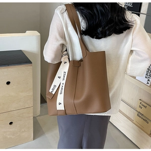 Detail of brown lychee grain tote bag with white lettered ribbon and soft leather texture