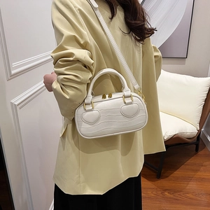 White crocodile pattern handbag with heart decor and gold hardware worn by a model