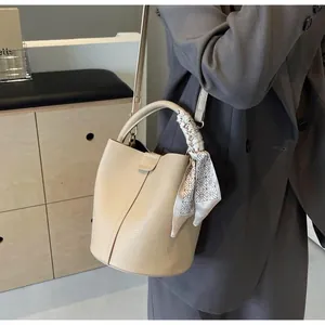 Détail du sac seau en cuir beige avec poignée décorée d'un foulard en soie géométrique