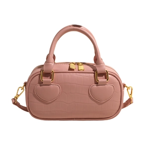 Pink crocodile pattern handbag with heart patches and golden zipper on white background