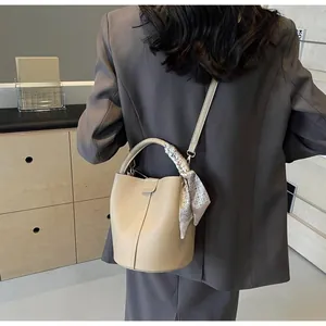 Détail du sac seau en cuir souple crème avec foulard en soie sur l'épaule du mannequin