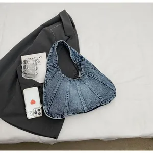 Detail of blue denim hobo bag featuring vertical stitching on white fabric backdrop