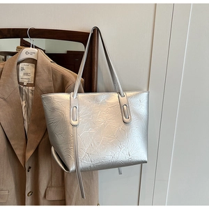 Detailed view of silver metallic tote bag with pleated texture hanging on a brown blazer