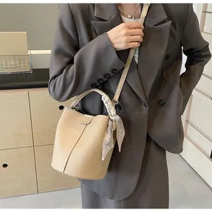 Détail du sac seau en cuir beige avec anse en foulard de soie sur une étagère en bois