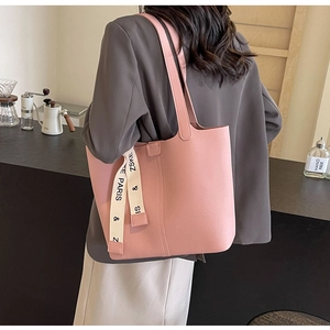 Detail of pink lychee leather tote bag featuring a decorative ribbon with letter prints