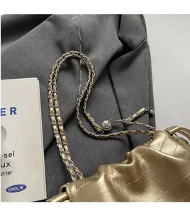 Detail of gold pleated cloud bag showing woven chain strap and adjustable metal ball