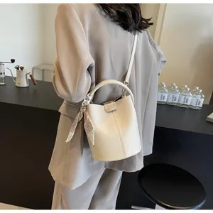 Détail d'un sac seau en cuir beige avec foulard en soie porté par un mannequin chic