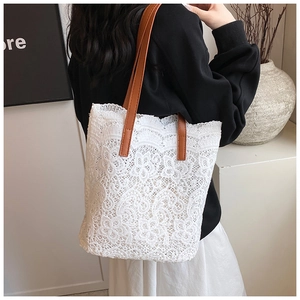 Detail of white lace tote bag with floral cutout patterns and brown leather handles
