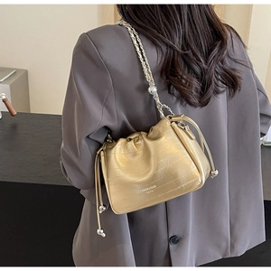 Detail of a gold metallic bucket bag with drawstring closure and silver chain strap