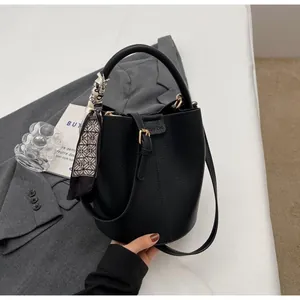 Détail du sac seau en cuir grainé noir avec foulard en soie et boucle métallique chic
