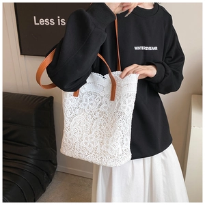 Detail of white lace tote bag with brown leather handles and floral crochet texture