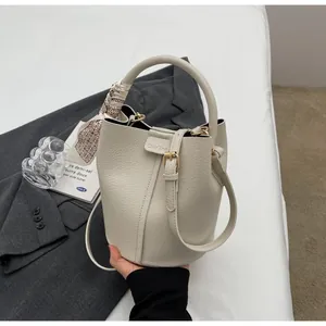 Détail du sac seau blanc cassé avec texture litchi et foulard en soie sur un blazer gris