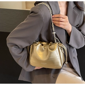 Detail of gold bucket bag with pleated texture, cloud closure and metal chain strap