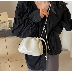 Detail of white crocodile texture bucket bag with chain strap worn by a model