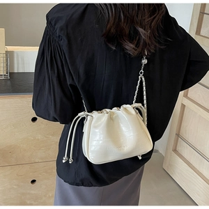 Detail of cream bucket bag showing crocodile texture and delicate chain strap on model