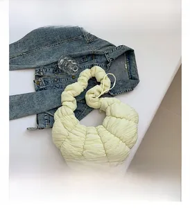 Détail du sac à bandoulière plissé crème en forme de croissant sur une surface marbrée