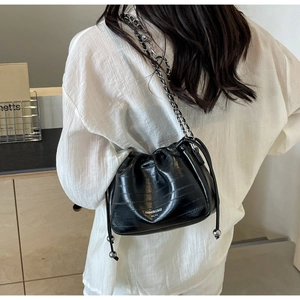 Detail of black patent leather bucket bag with drawstring closure and silver metal accents