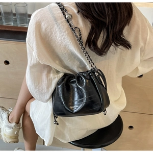 Detail view of black crocodile pattern leather bucket bag with silver chain strap