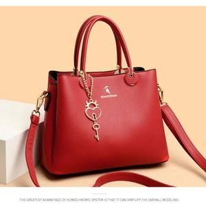 Detail of red lychee grain leather tote bag with gold heart keychain on geometric props