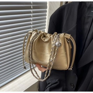 Detail of golden metallic drawstring bucket bag with silver chain and sphere charm