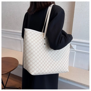 Dettaglio di una borsa tote crema con motivi monogramma marroni e doppi manici