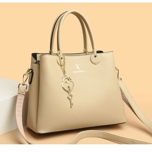 Close-up of beige lychee grain leather handbag with gold heart charm and brand logo
