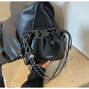 Detail of black drawstring bucket bag with crocodile embossing and silver metal chain strap