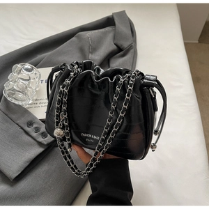 Detail of black drawstring bucket bag with silver chain strap and faux leather texture