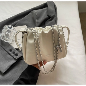 Detail of white crocodile texture ruched chain bucket bag on grey suit background
