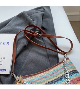 Detail of colorful woven straw bucket bag with brown leather strap and silver chain links