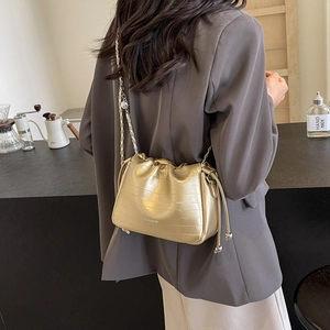 Golden chain strap bucket bag with textured finish shown on shoulder in lifestyle setting