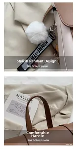 Detail of a brown leather tote with a white pompom charm and logo webbing handle strap