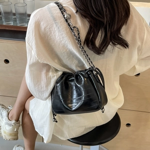 Fashionable black drawstring bucket bag with silver chain strap shown in a lifestyle scene