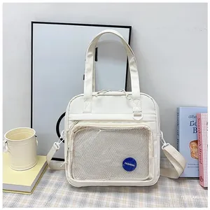 Detail of cream nylon tote bag featuring a clear mesh pocket and fashion patch logo