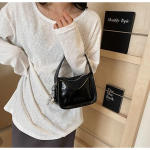 Gros plan sur un sac sous le bras en cuir noir brillant avec pendentif boule argentée