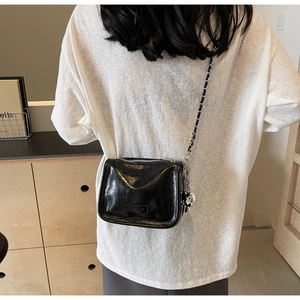 Détail du sac bandoulière en cuir noir brillant avec breloque ours argentée et logo