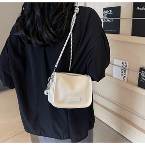 Détail du sac à bandoulière blanc cassé avec bandoulière tressée et pendentif argenté