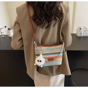 Close-up of colorful striped straw bucket bag with leather strap and plush doll charm