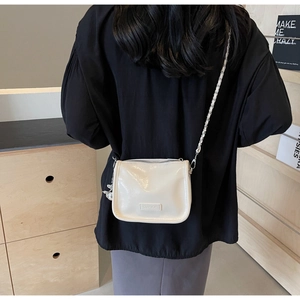 Détail d'un sac sous le bras blanc crème brillant avec chaîne en métal porté par un mannequin