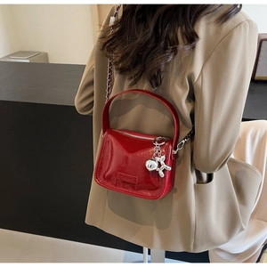 Détail du sac à bandoulière en cuir verni rouge avec chaîne argentée et breloque chien