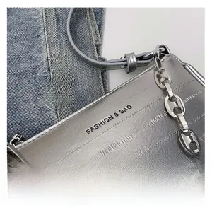 Détail d'un petit sac argenté avec bandoulière chaîne épaisse et logo embossé