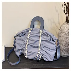 Close-up of light blue pleated nylon shoulder bag with adjustable strap and drawstring details