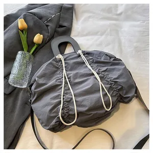 Detail of a dark gray pleated handbag with round handles and white decorative ropes