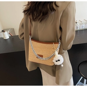 Close-up of straw bucket bag with silver metal chain and white plush pendant detail
