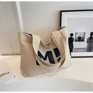 Dettaglio della borsa tote in tela crema con stampa M! blu e tracolla larga