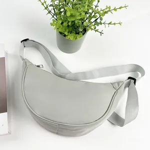 Vue détaillée du sac demi-lune en nylon gris clair sur un bureau blanc minimaliste