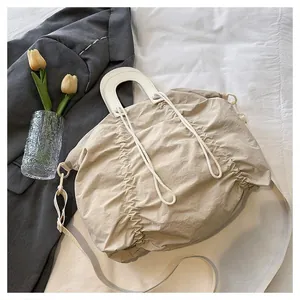 Detail of pleated tote bag in beige with leather ring handles and adjustable shoulder strap