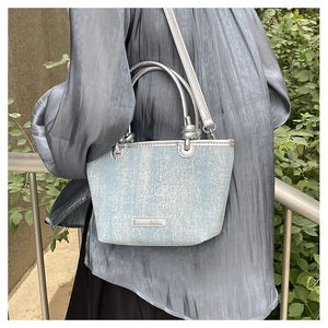 Detail view of denim texture handbag with silver metal handle and adjustable strap